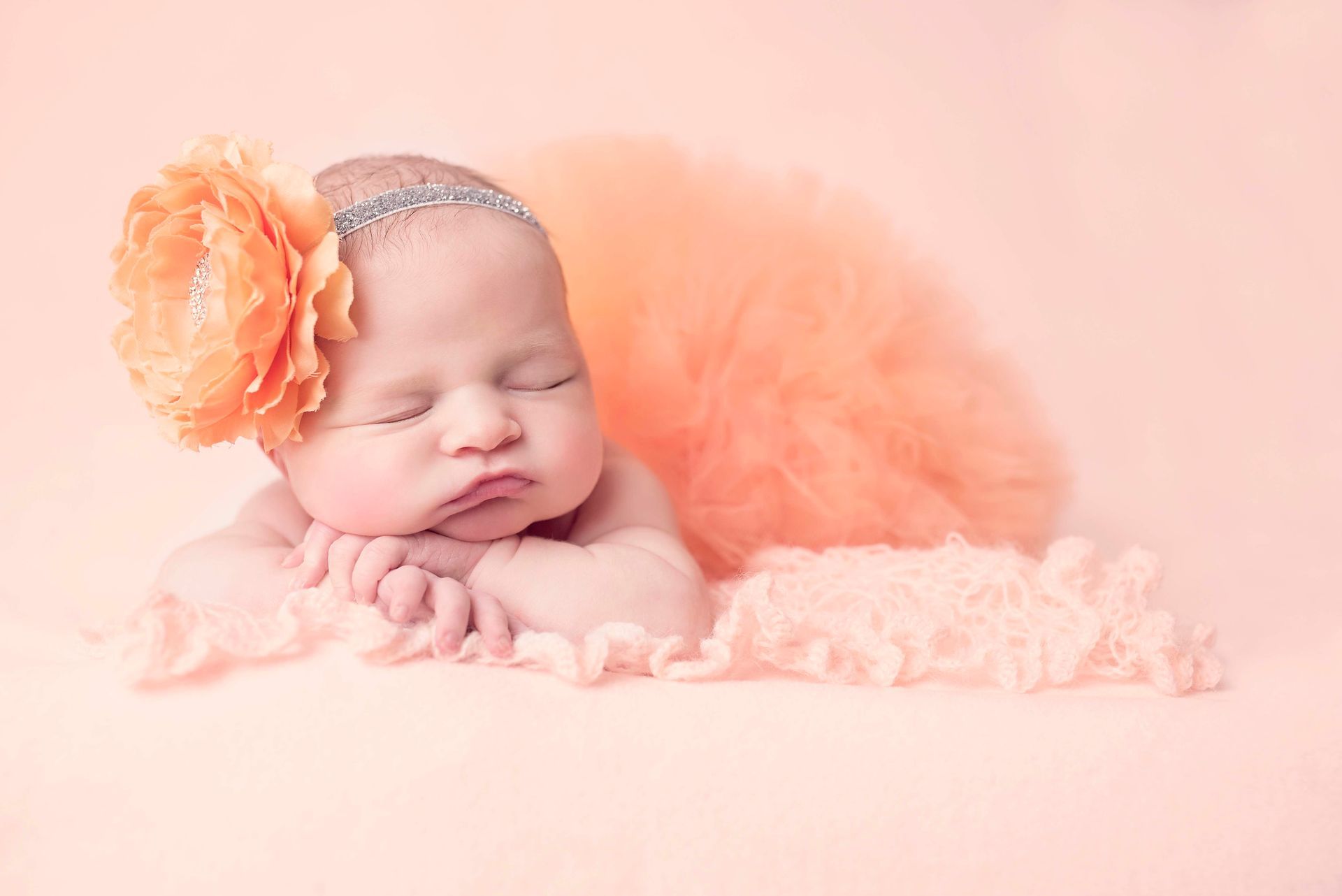 Sleeping newborn with orange flower headpiece and matching fluffy backdrop.
