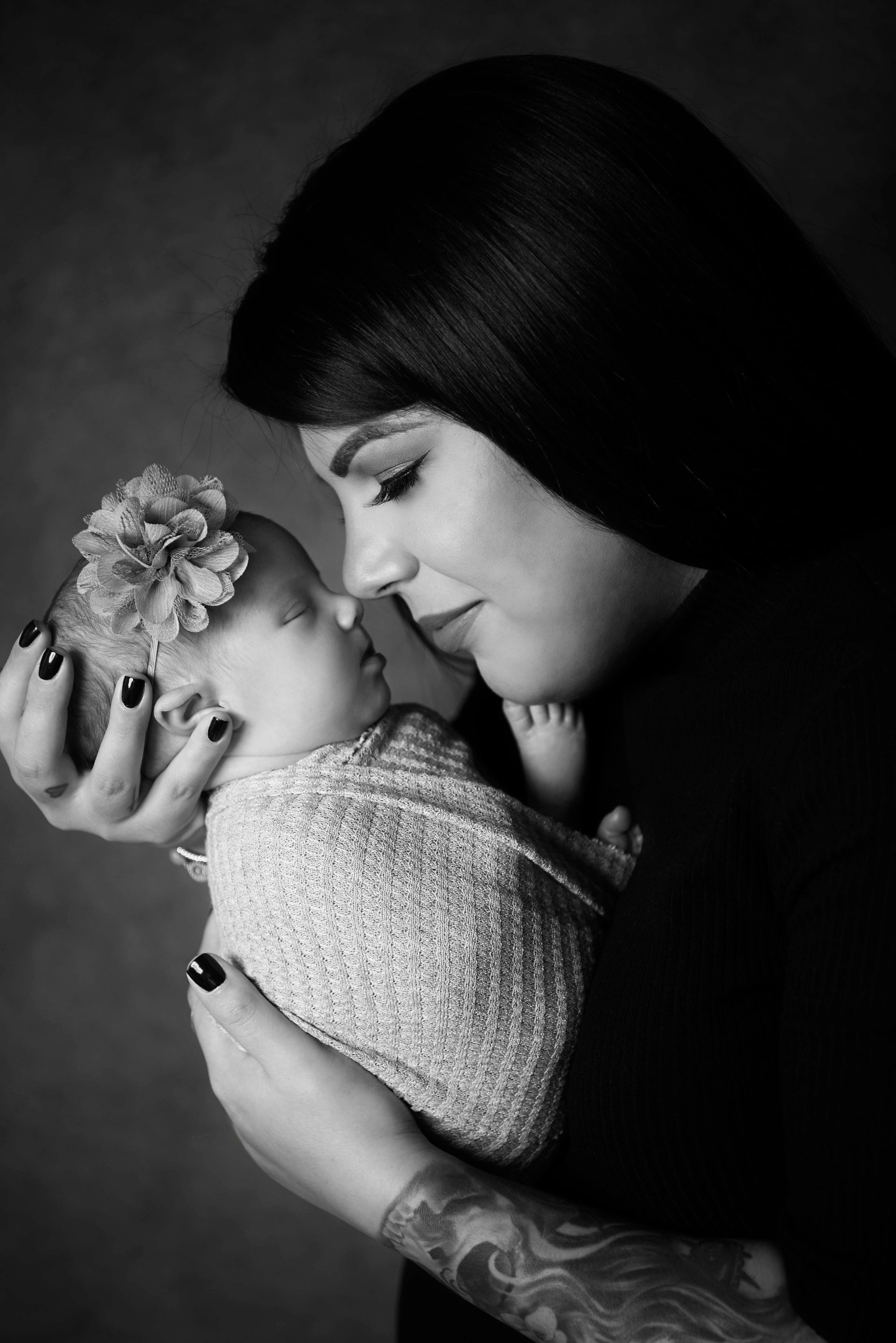 Mother holding a swaddled newborn, nose to nose. Black and white portrait, studio setting.
