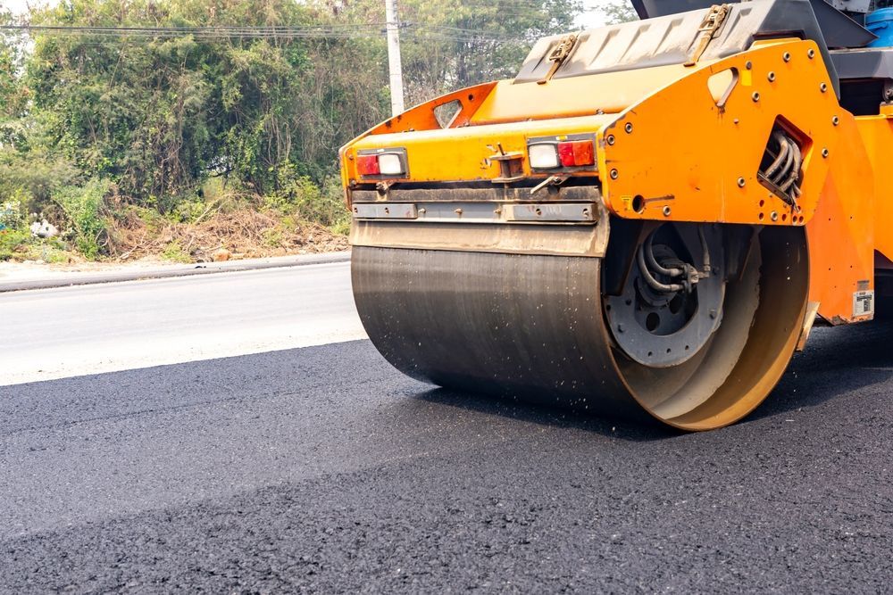 Orange road roller compacting fresh asphalt on a road near trees