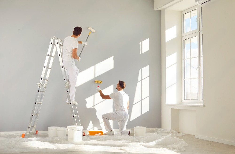 two men are painting a wall in an empty room .