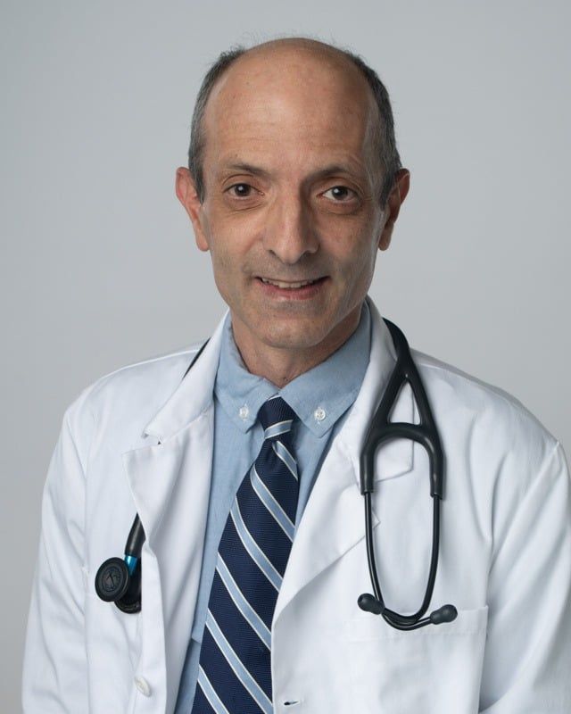 A doctor wearing a white coat and tie with a stethoscope around his neck.