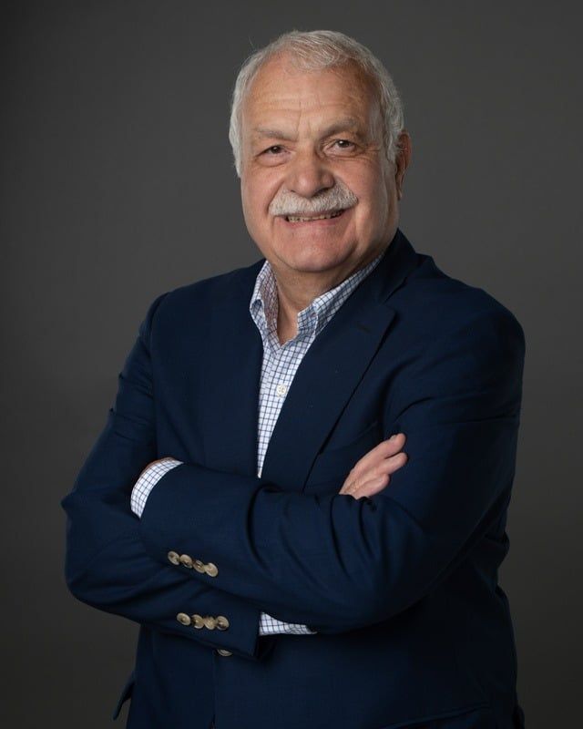 A man in a blue suit is standing with his arms crossed.
