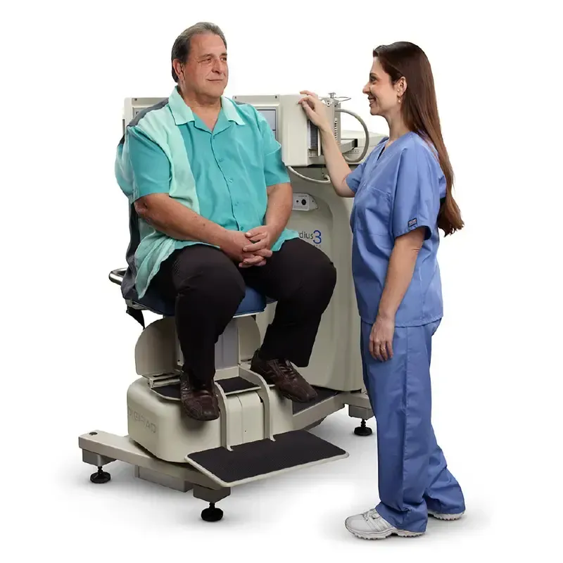 Man seated in medical testing chair, nurse standing nearby, smiling. Medical office setting.