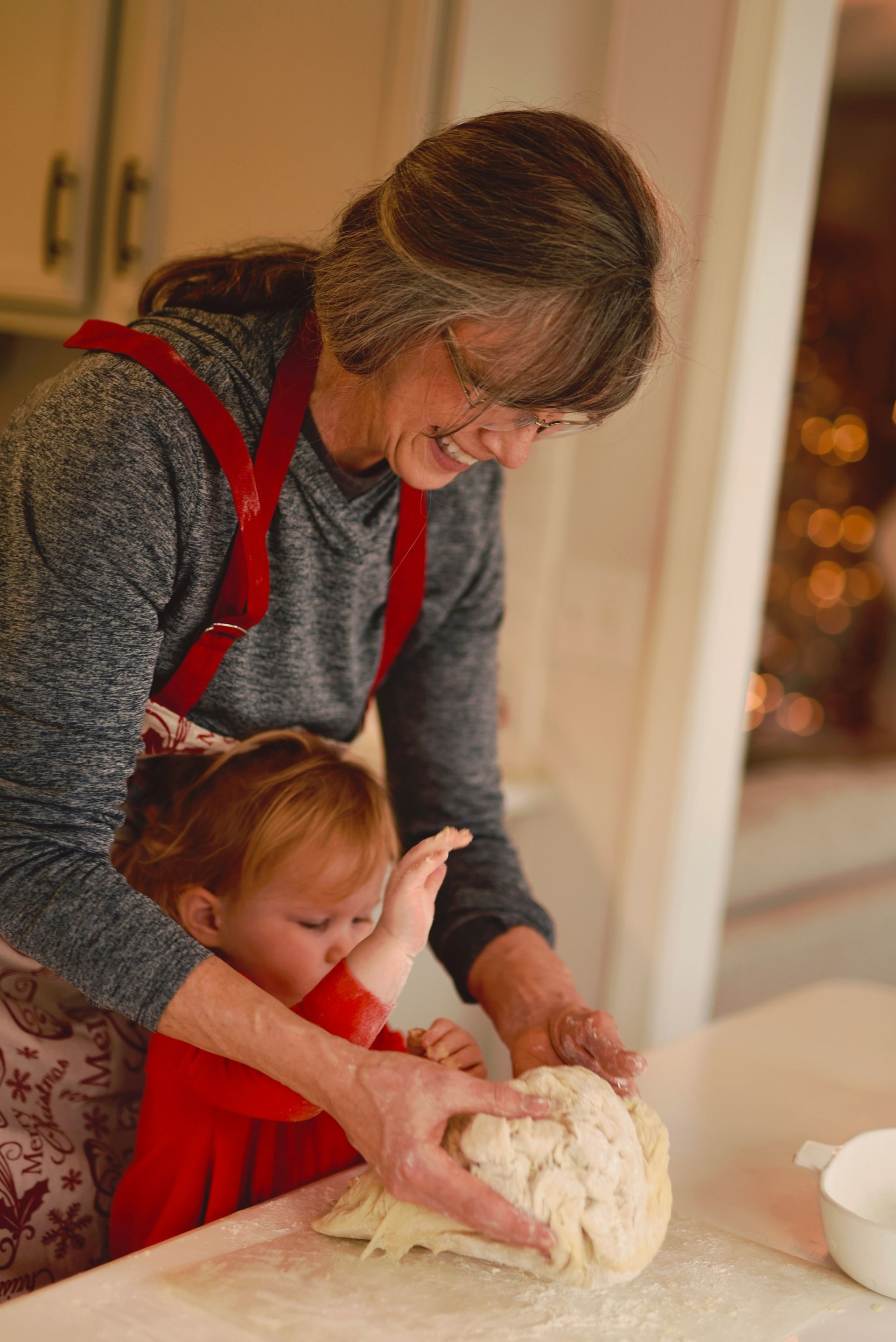 Woman and child baking together, pressing dough on a table, kitchen setting.
