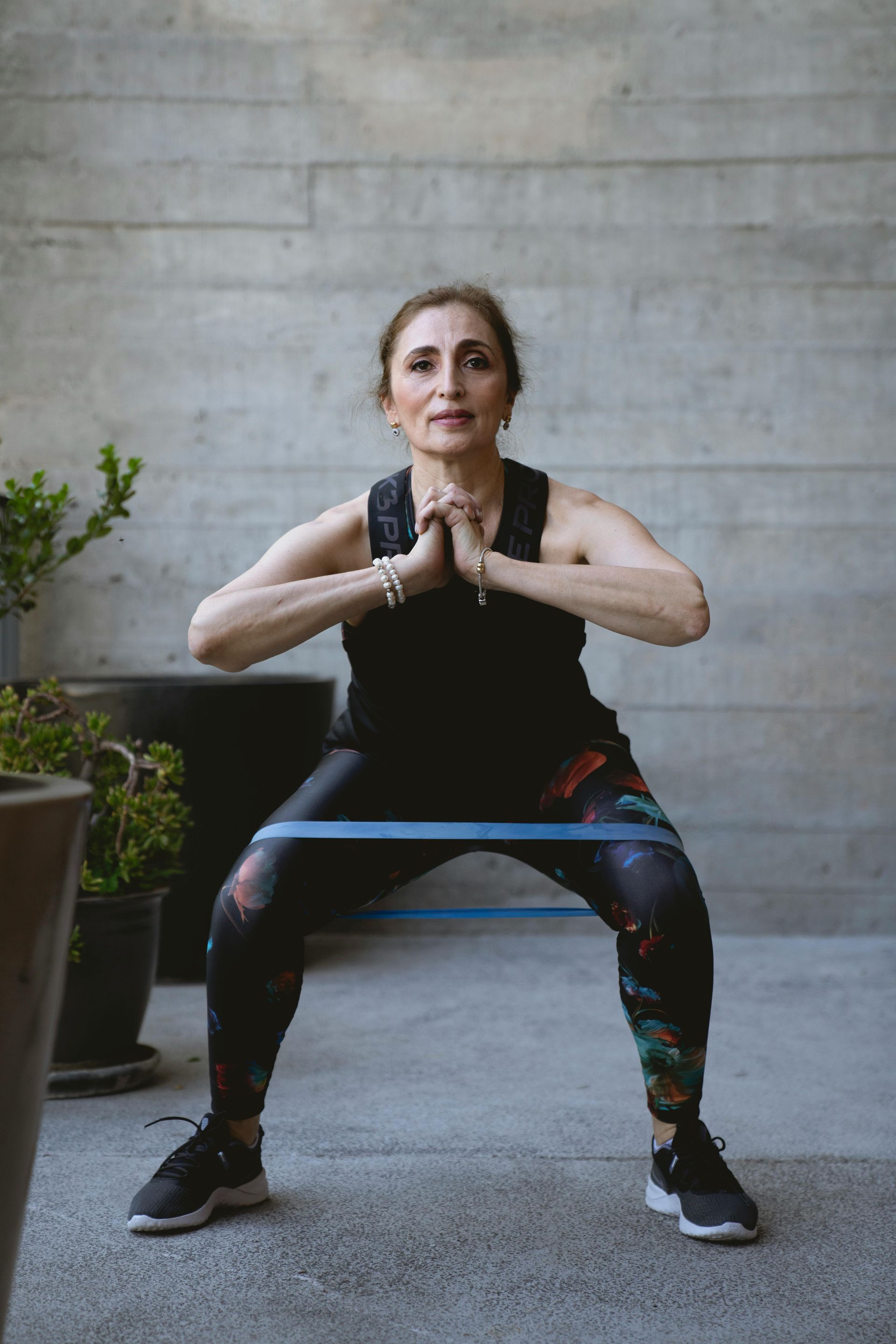Woman doing a squat with a resistance band outdoors, hands in prayer pose, wearing workout clothes.