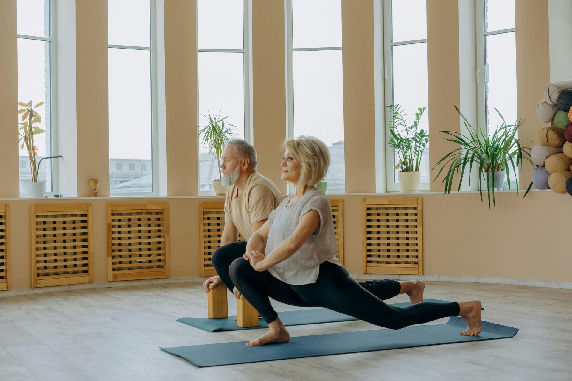 Two people in yoga poses on mats in a bright room.