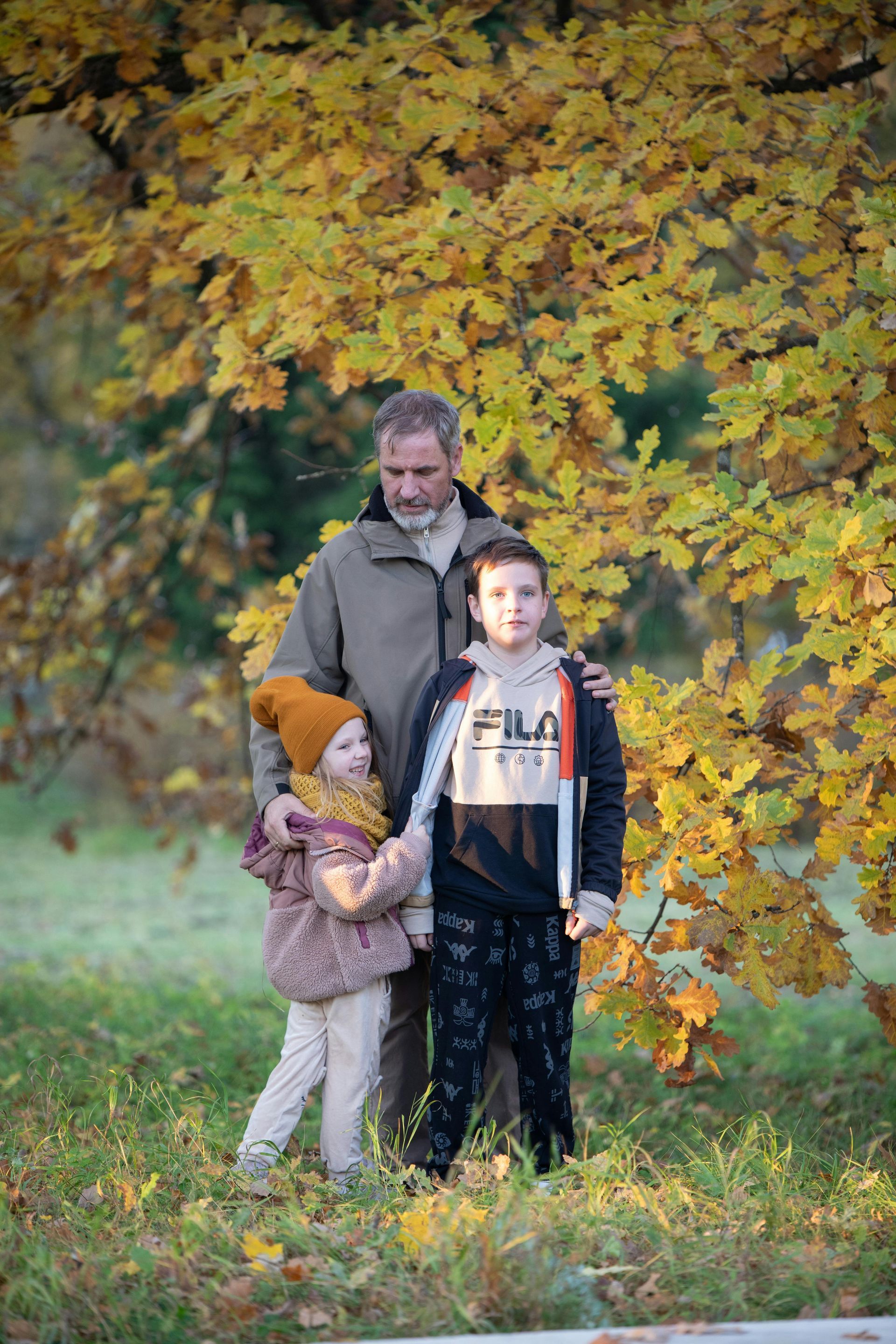 A man and two children are standing in front of a tree in a park.