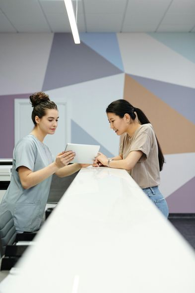 Two women are standing at a counter looking at a tablet.
