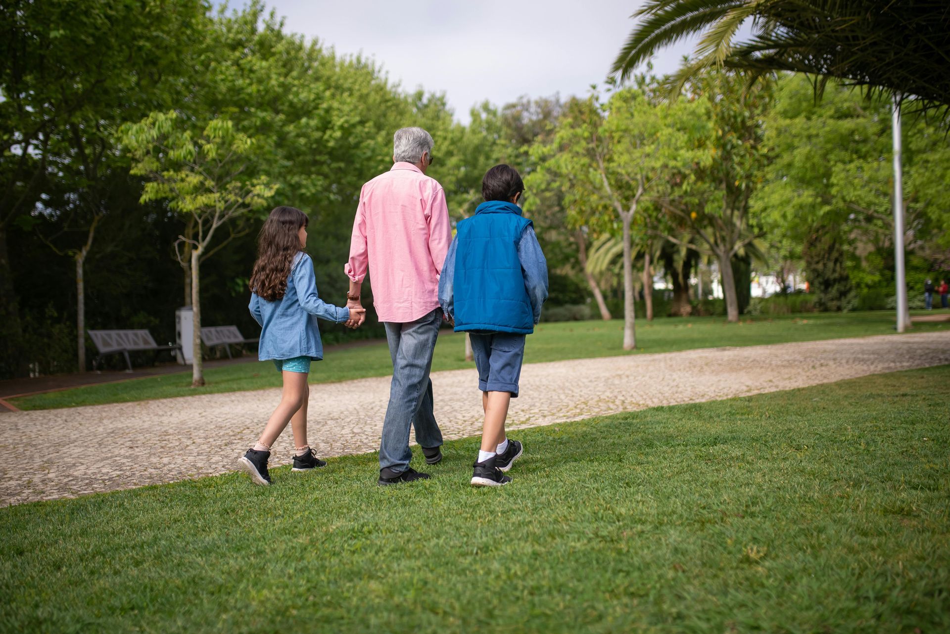 A man and two children are walking in a park holding hands.
