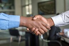 Two hands clasped in a handshake. One arm in blue shirt, the other in white. Blurred office setting.