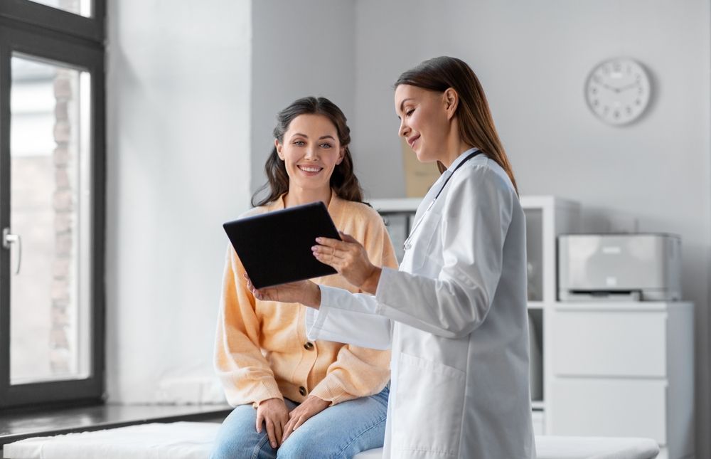 Doctor in white coat showing tablet to smiling patient in a bright room.