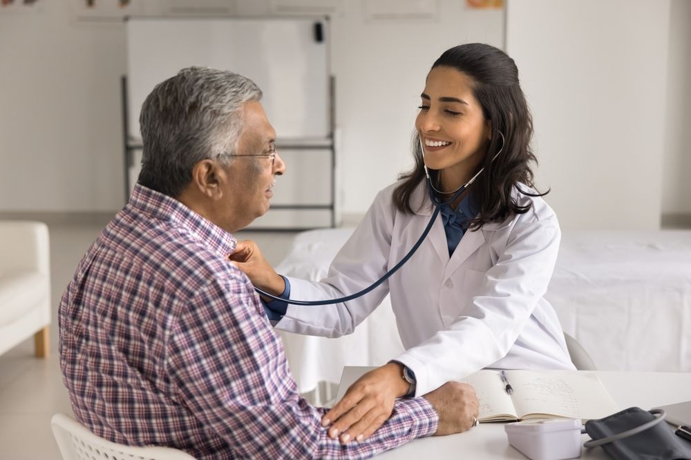 Doctor examining a patient's chest with a stethoscope in a medical office.