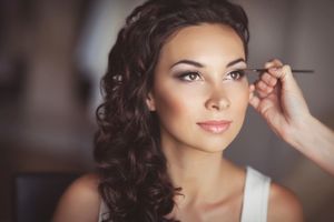 Una maquilladora aplica delineador de ojos a una mujer con cabello castaño