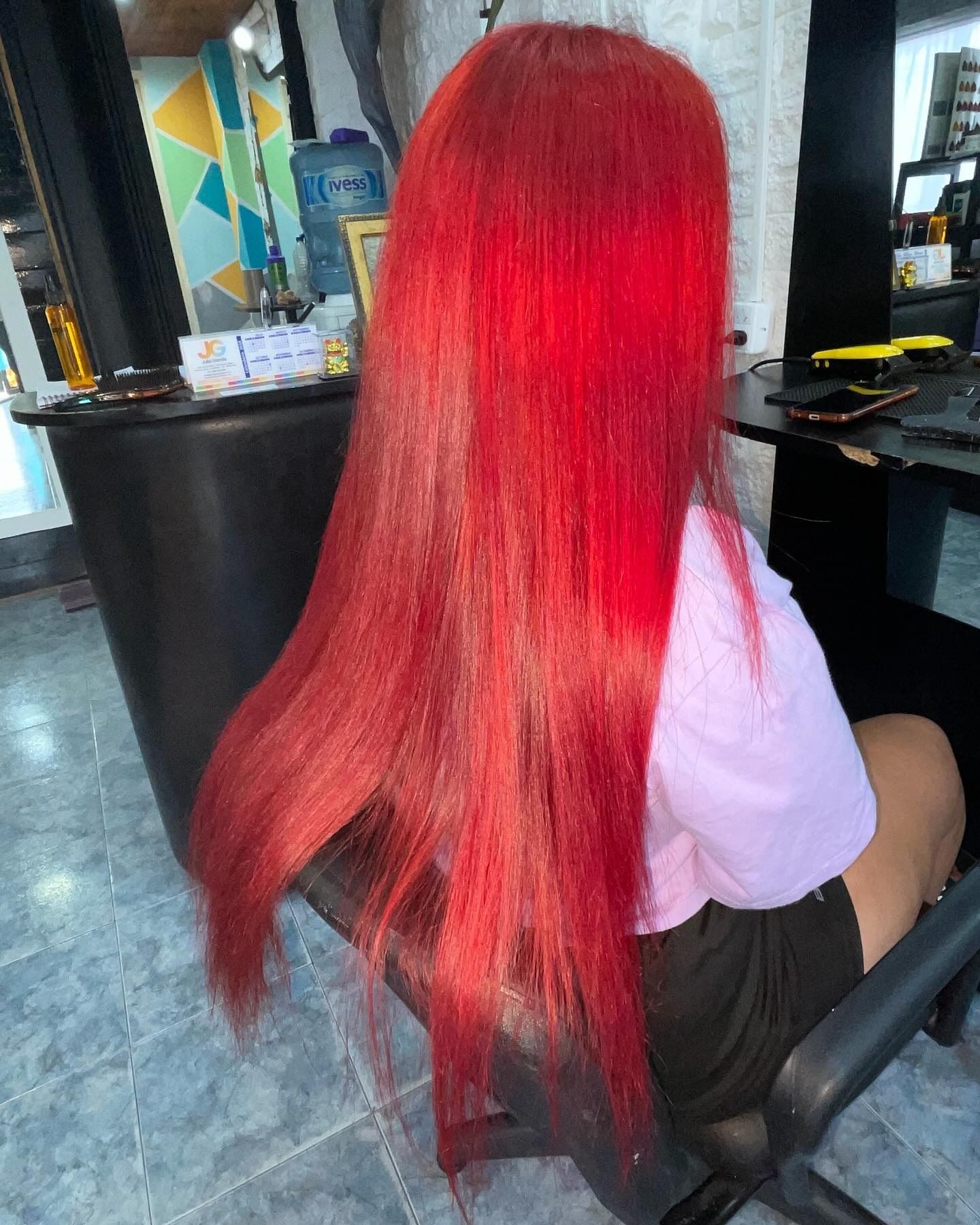 Una persona con cabello largo y de un rojo intenso está sentada en una silla en un salón de belleza.
