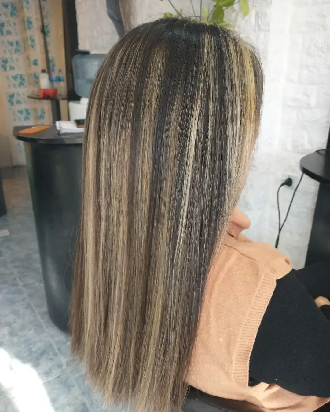 Vista posterior de cabello liso con reflejos castaños y rubios en un salón de belleza.