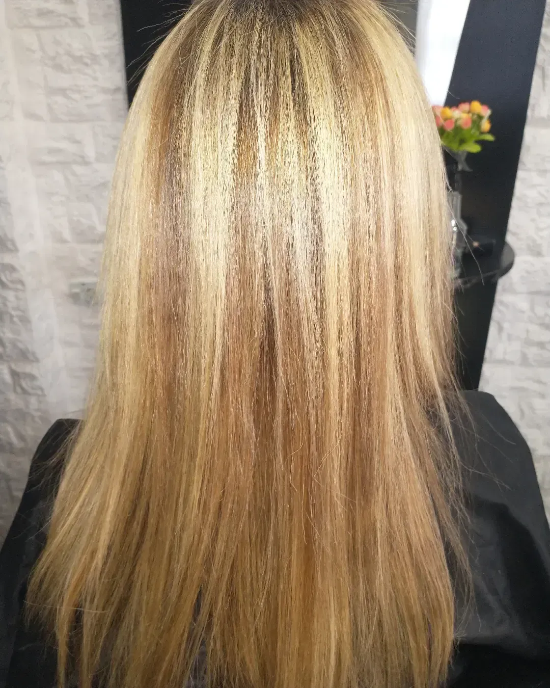 Vista posterior de una melena larga y rubia con daños visibles, encrespamiento y reflejos en un salón de belleza.