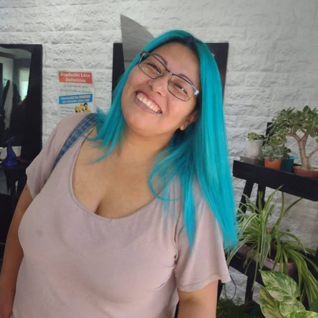 Una persona sonriente, con cabello de color verde azulado brillante y gafas