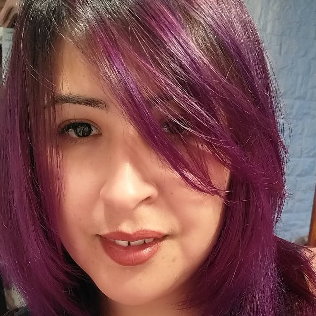 Una persona con cabello morado vibrante hasta los hombros y raíces oscuras, mirando al frente con expresión neutra.