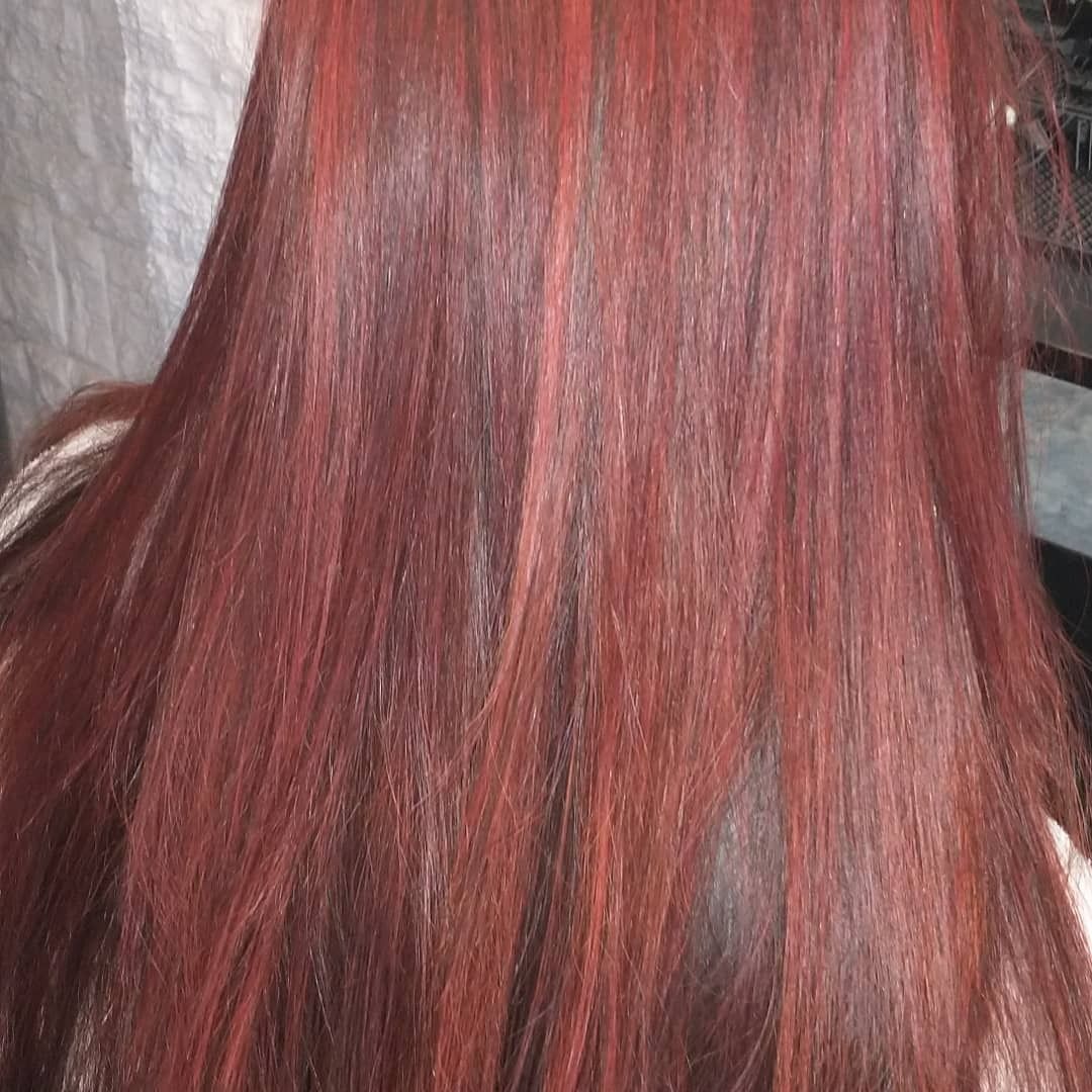 Primer plano de una melena lisa de color castaño rojizo con vibrantes reflejos rojos que caen por la espalda.