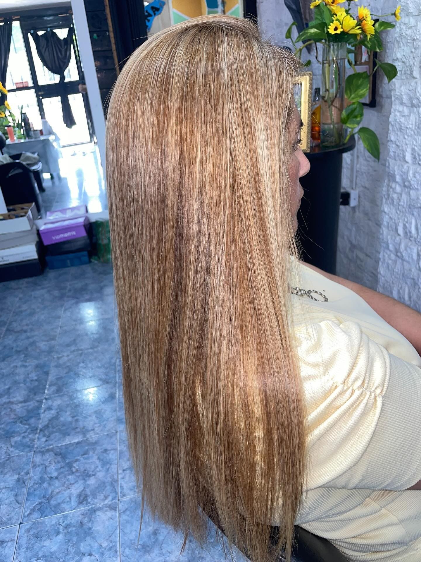 Vista de perfil de una persona con cabello largo, texturizado y rubio dorado en un salón de belleza.