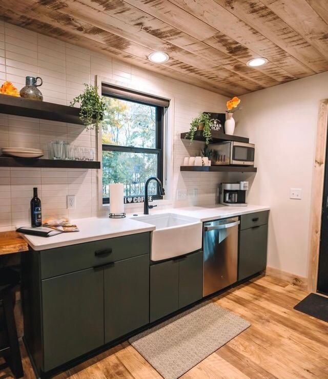 A kitchen with green cabinets , stainless steel appliances , a sink and a window.