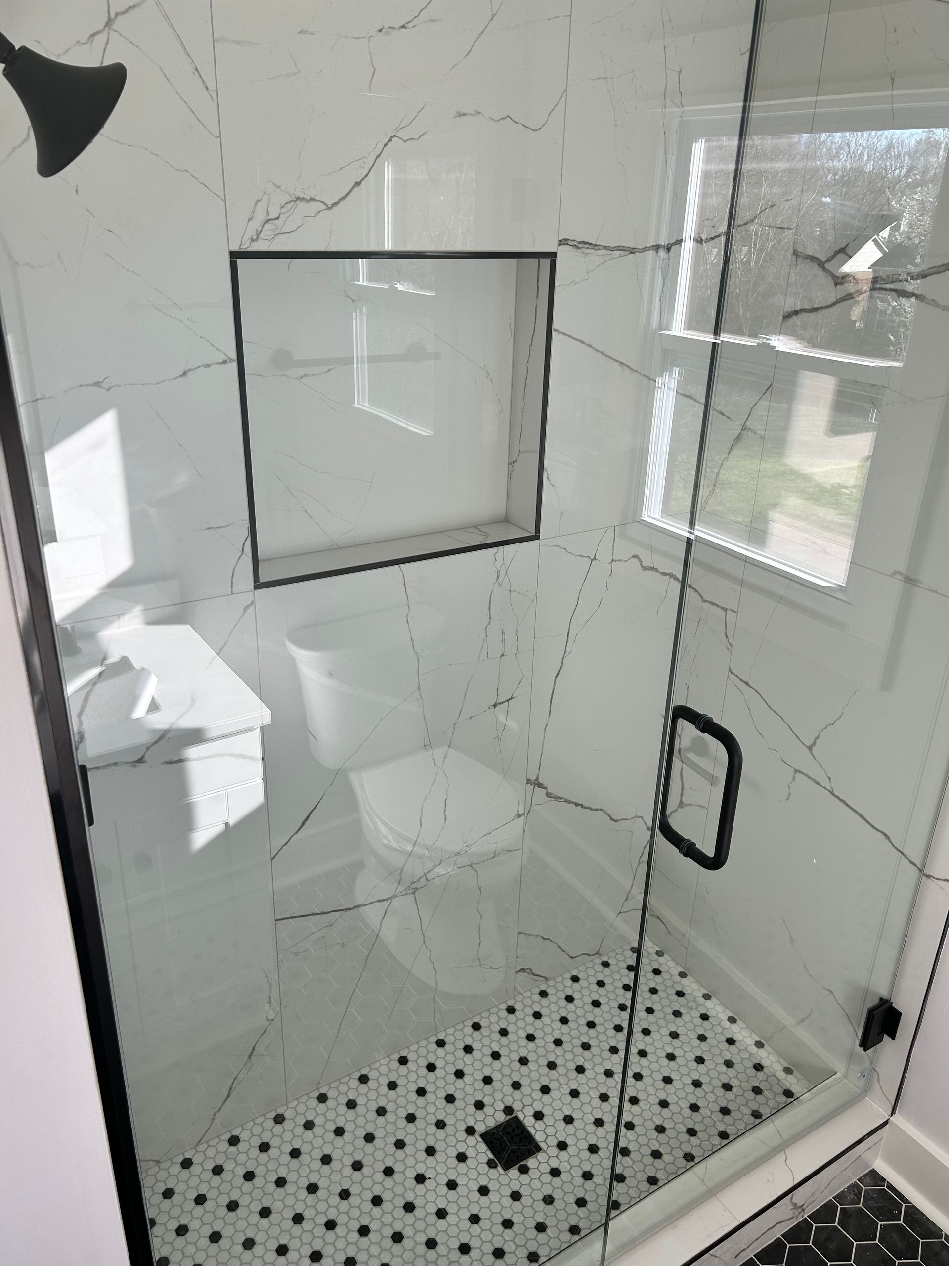 A bathroom with a walk in shower with a black and white tile floor.