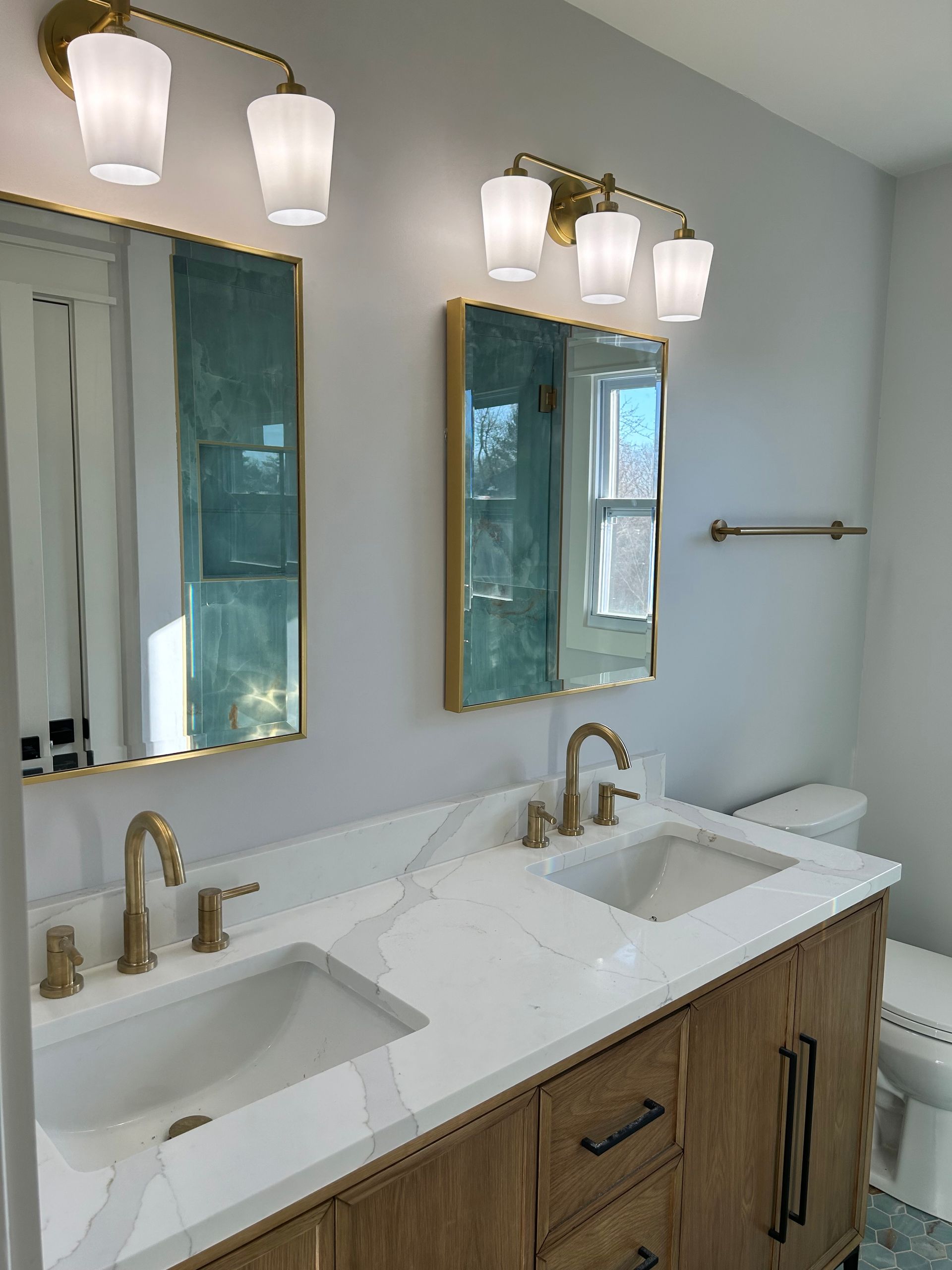 A bathroom with two sinks , two mirrors and a toilet.