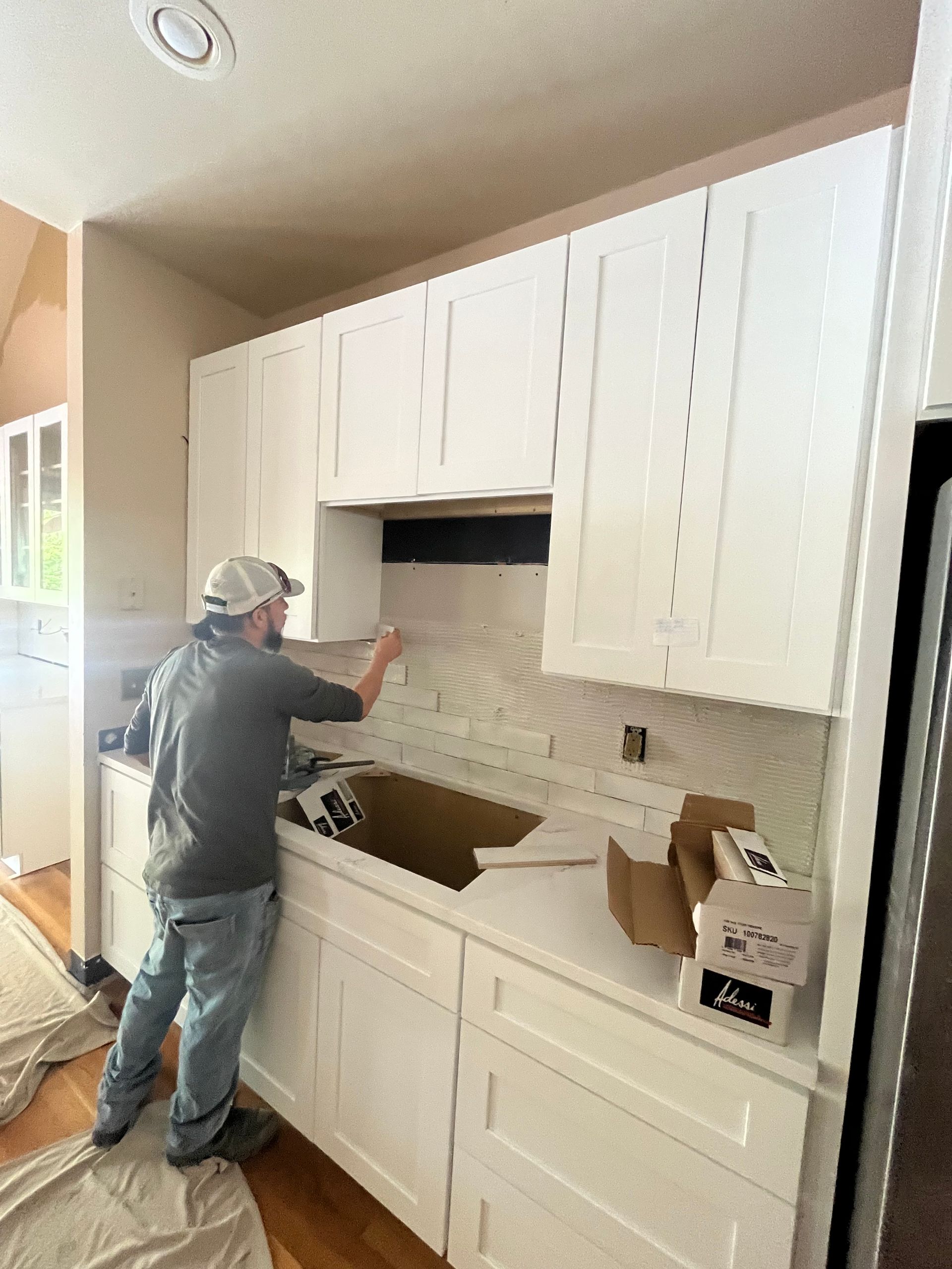 A man is working on a kitchen with white cabinets and a sink.