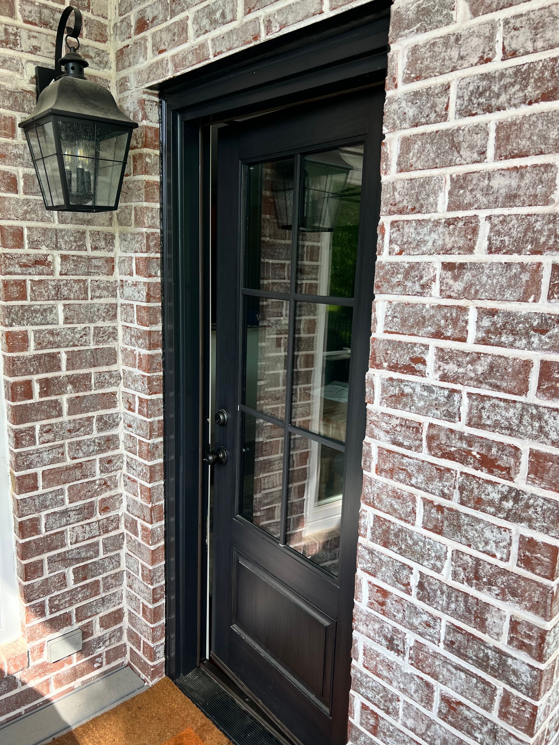 A black door is on a brick wall next to a lamp.