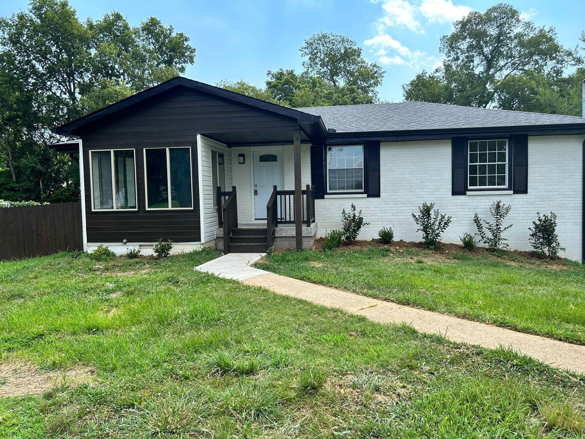 A white house with a brown roof and black shutters is sitting on top of a lush green lawn.