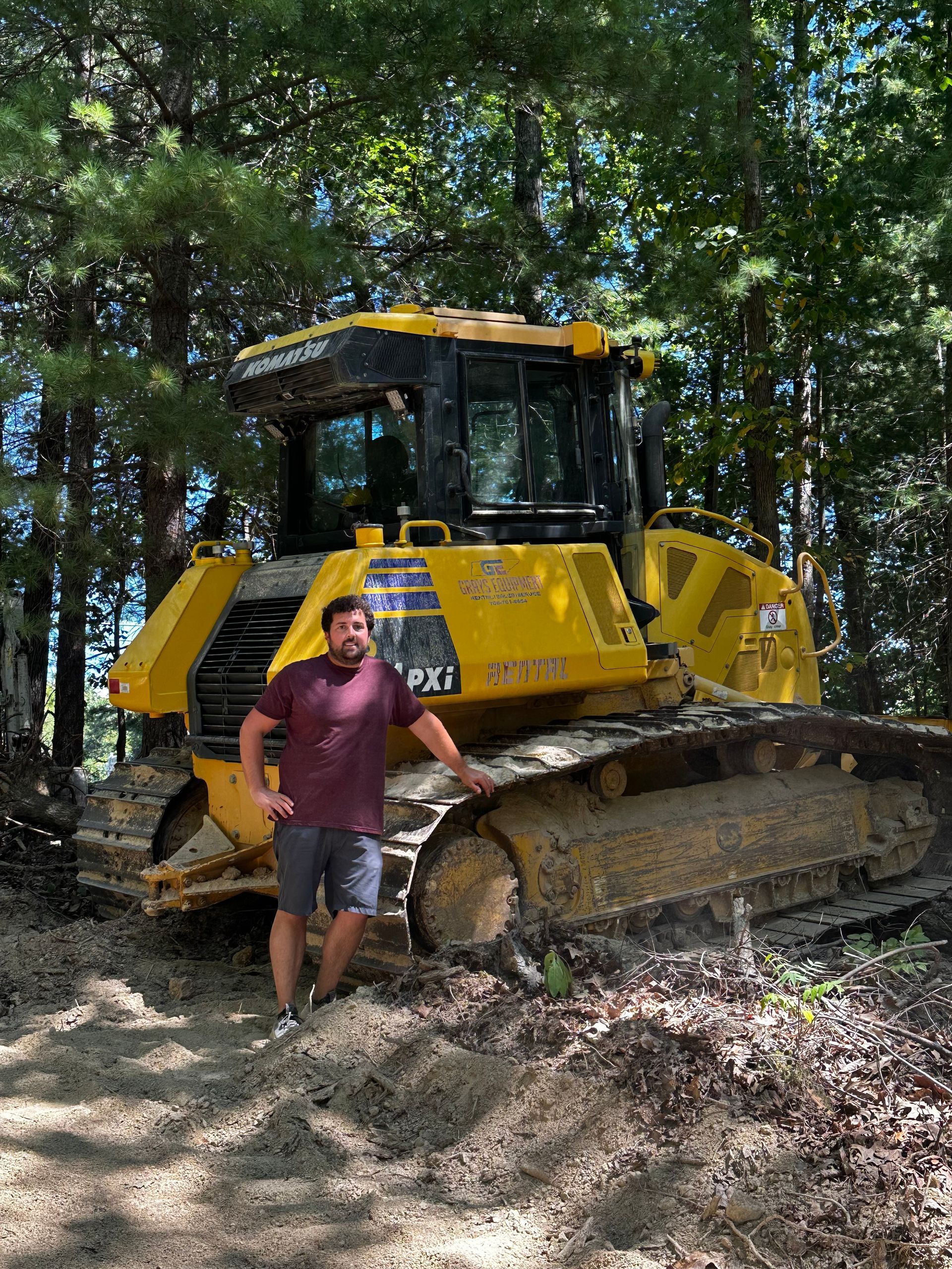 A man is standing in front of a bulldozer in the woods.