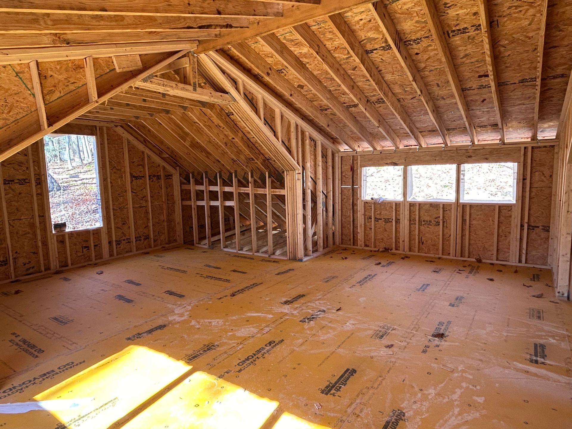 A room in a house under construction with wooden beams and windows.