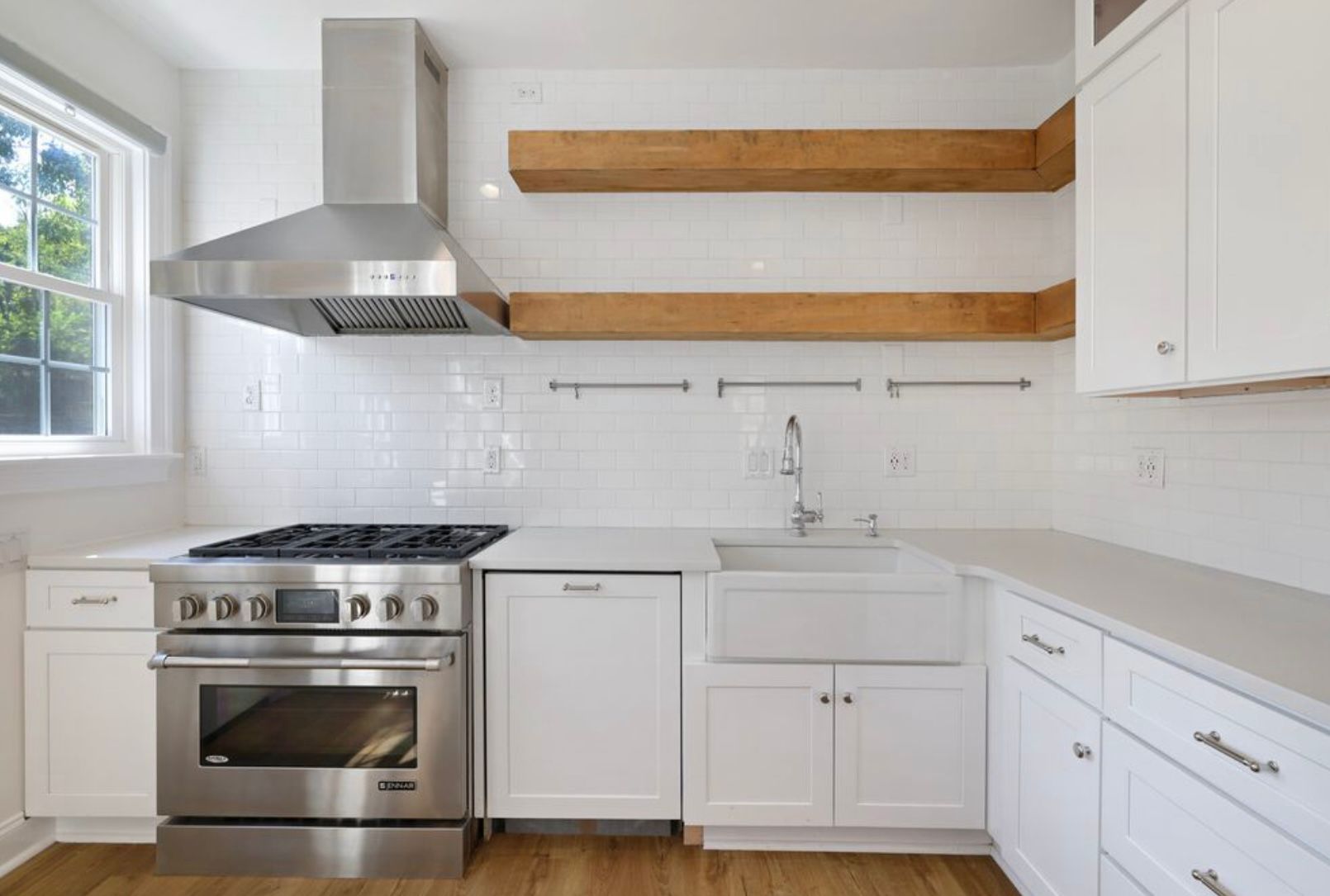 A kitchen with white cabinets , stainless steel appliances , a sink and a window.
