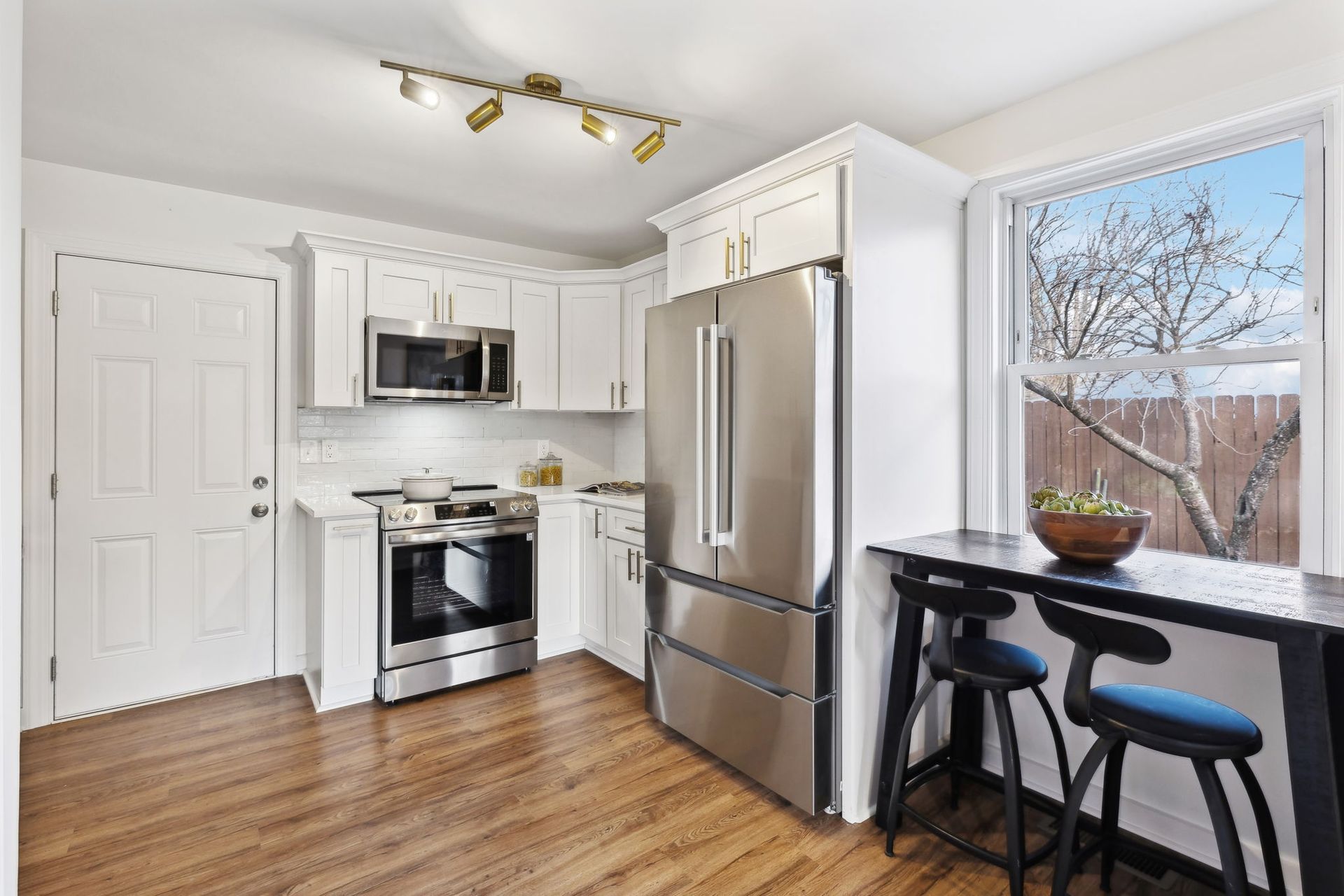 A kitchen with stainless steel appliances , white cabinets , hardwood floors and a window.