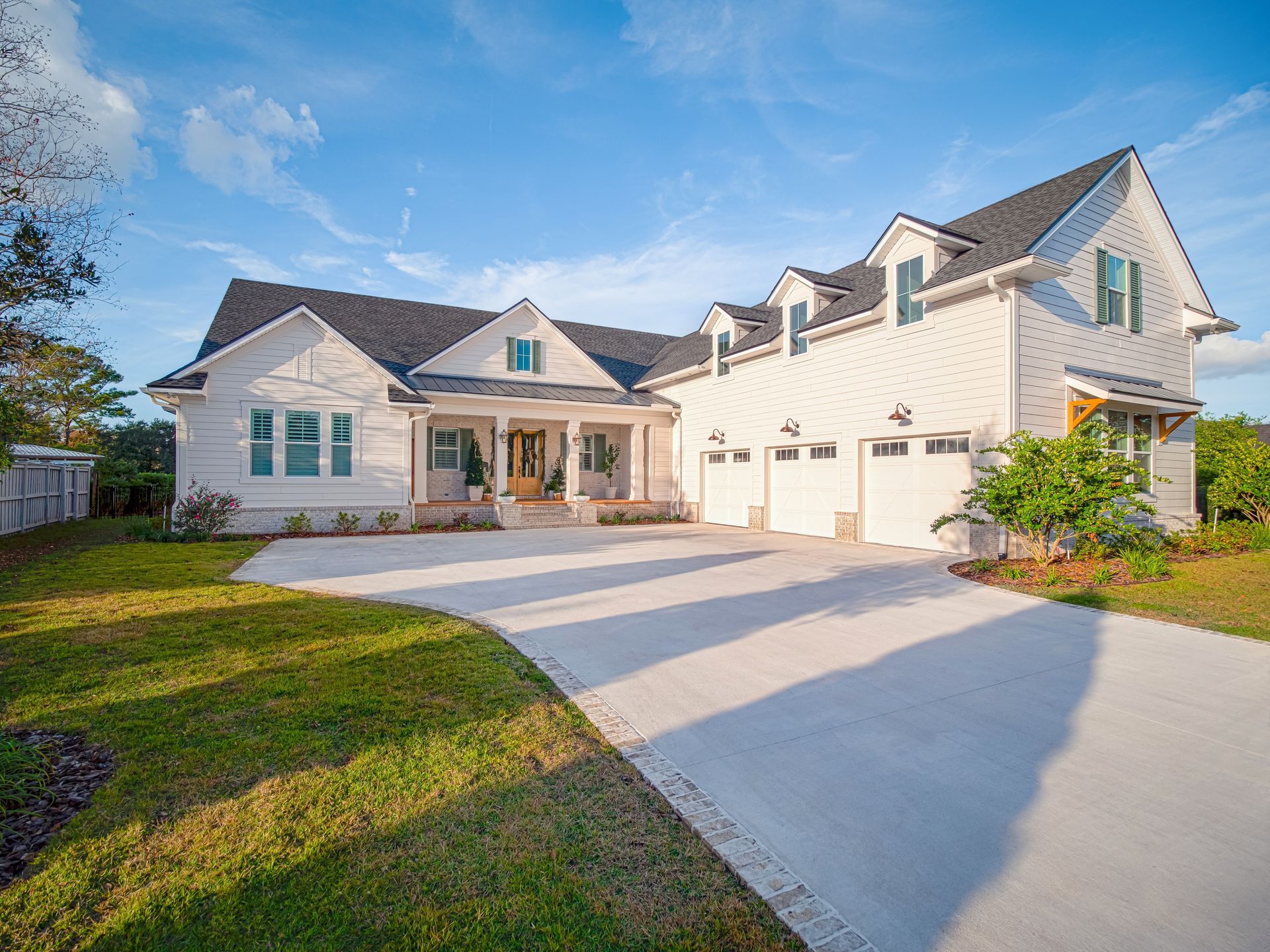 Large white suburban house with a driveway, front porch, and green lawn in bright daylight
