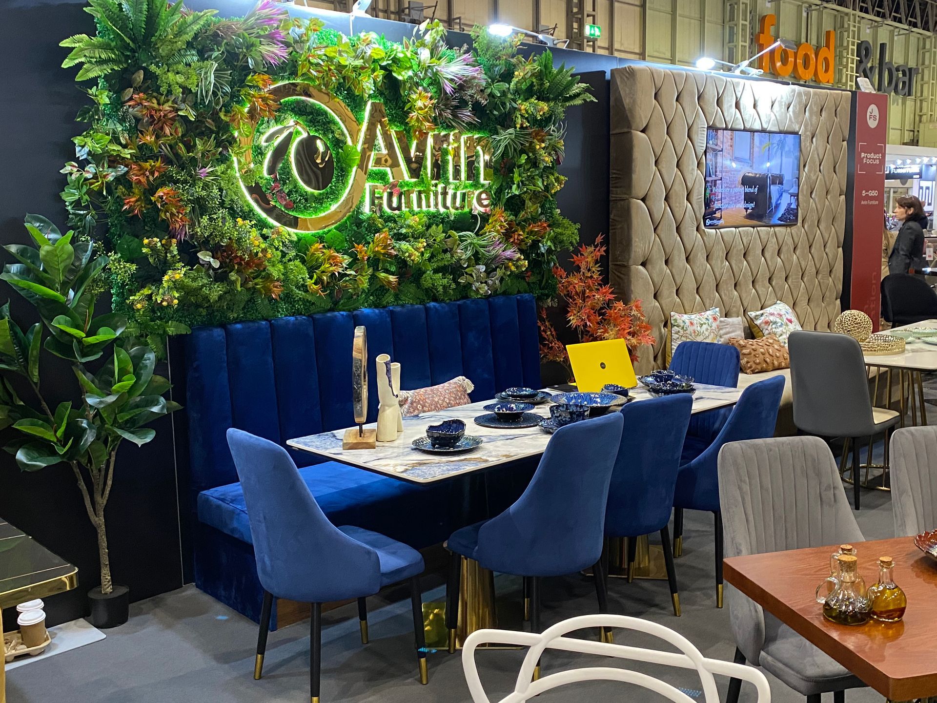 luxury comfortable restaurant specification dining table with blue velvet ocassional chairs and matching bench set in front of artificial living wall at the January Furniture Show 2024, NEC, Birmingham