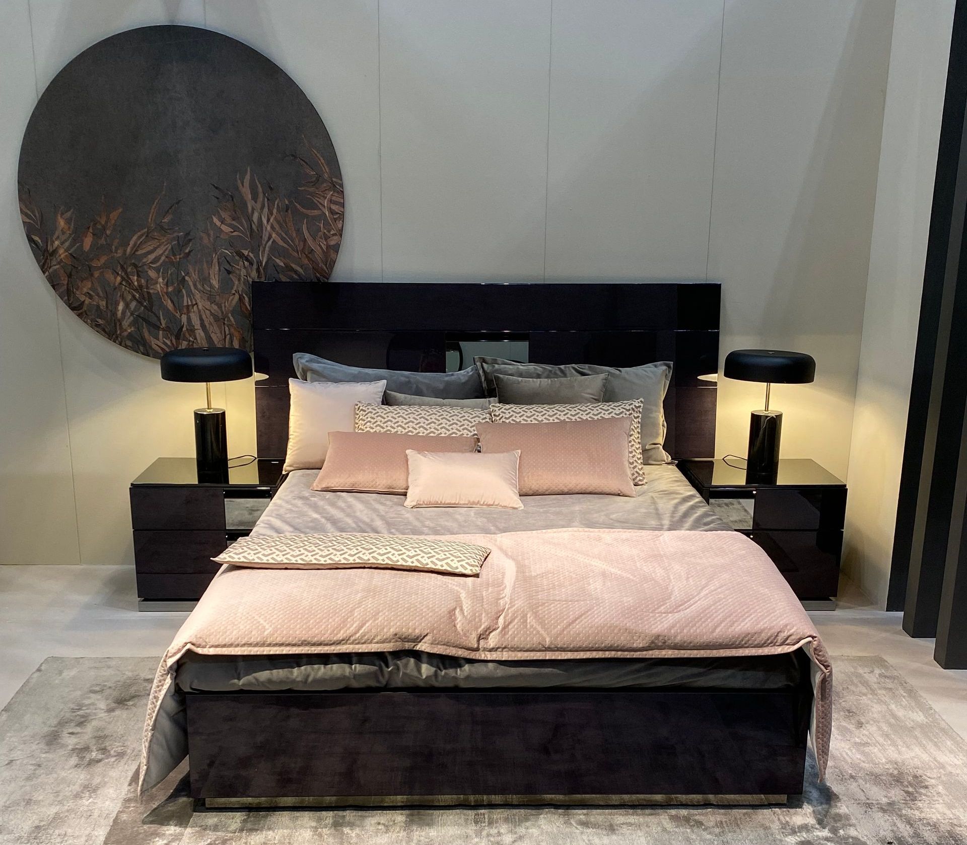 luxury with black headboard, pink and grey bedding and scatter cushions bed with two black side cabinets and domed lamps. A large circular wallart piece hangs on the wall behind. All at the January Furniture Show 2024, NEC, Birmingham