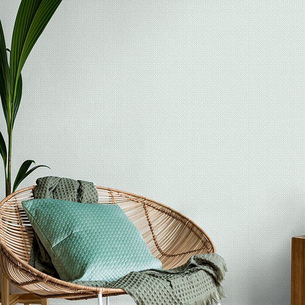 a wicker chair with two pillows and a blanket on it in front of a white wall .