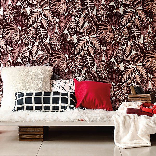 a couch with pillows on it in front of a wall with leaves on it