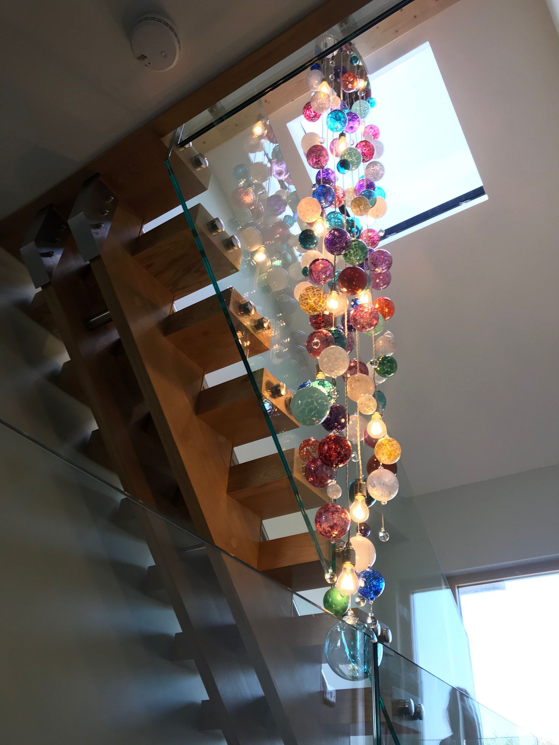 a staircase with a glass railing and a Roast Designs multi-coloured glass ball chandelier hanging from the ceiling