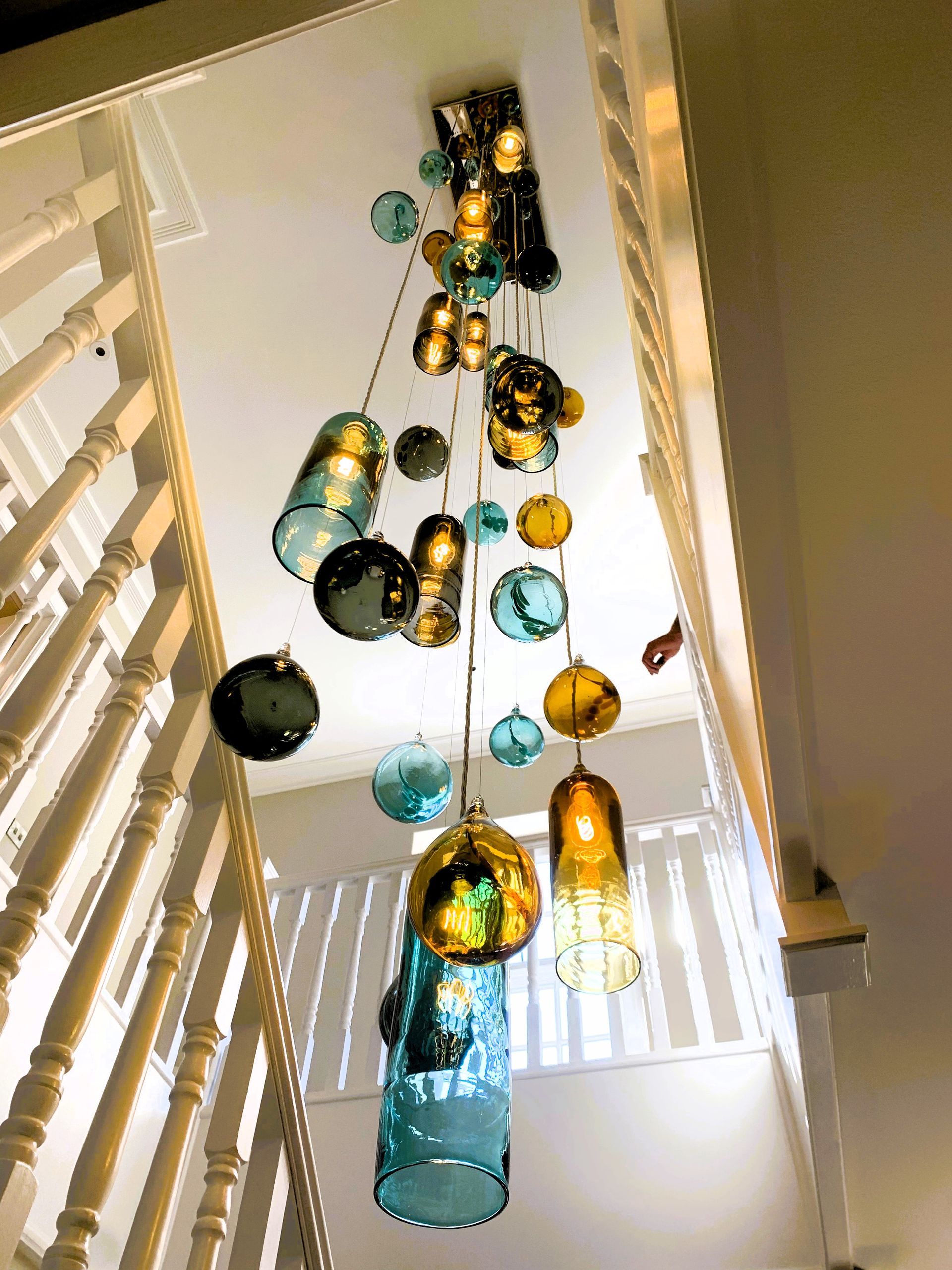 a staircase with a Roast Designs mixed glass ball and tube chandelier hanging from the ceiling