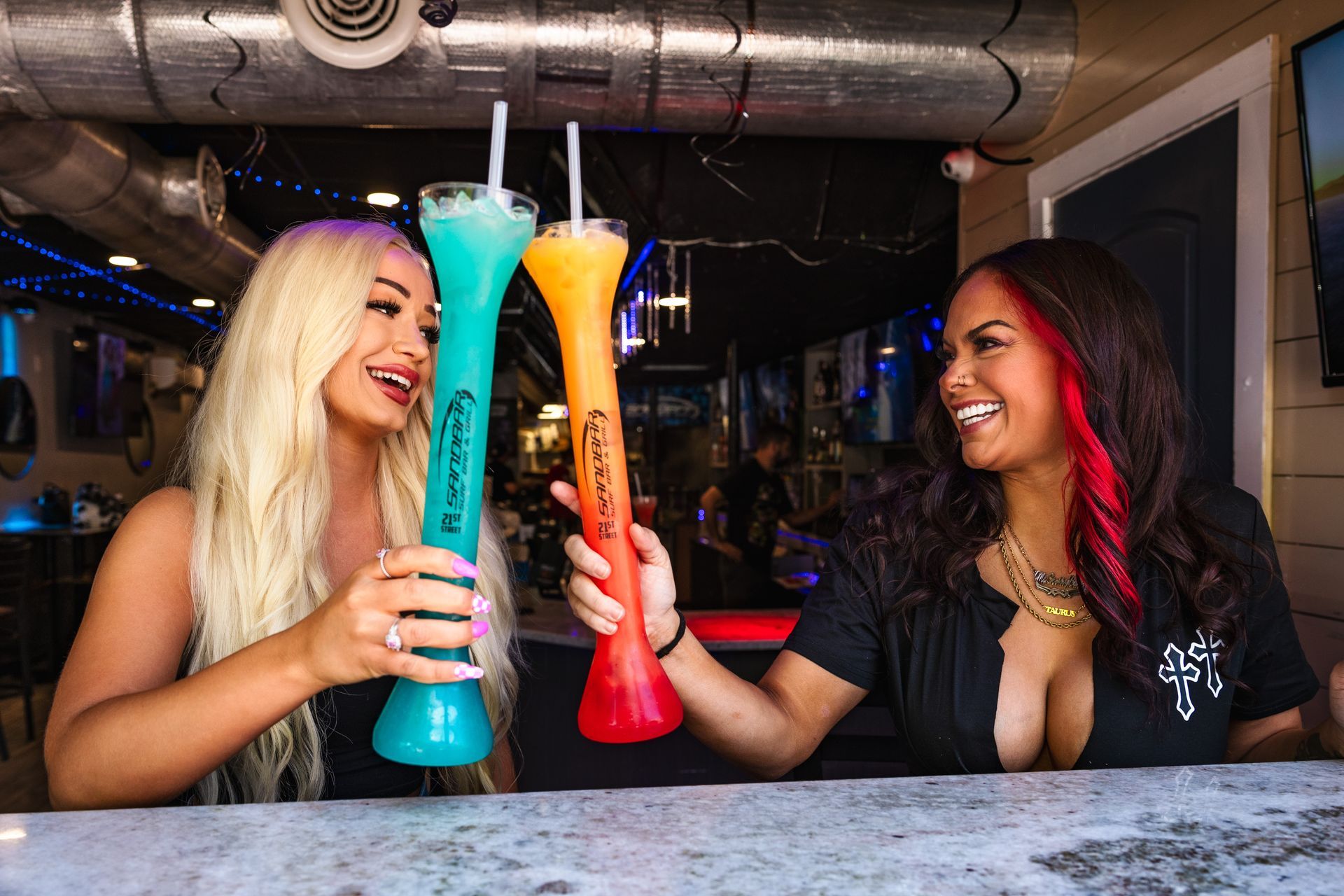 Two women are sitting at a bar holding tall drinks.