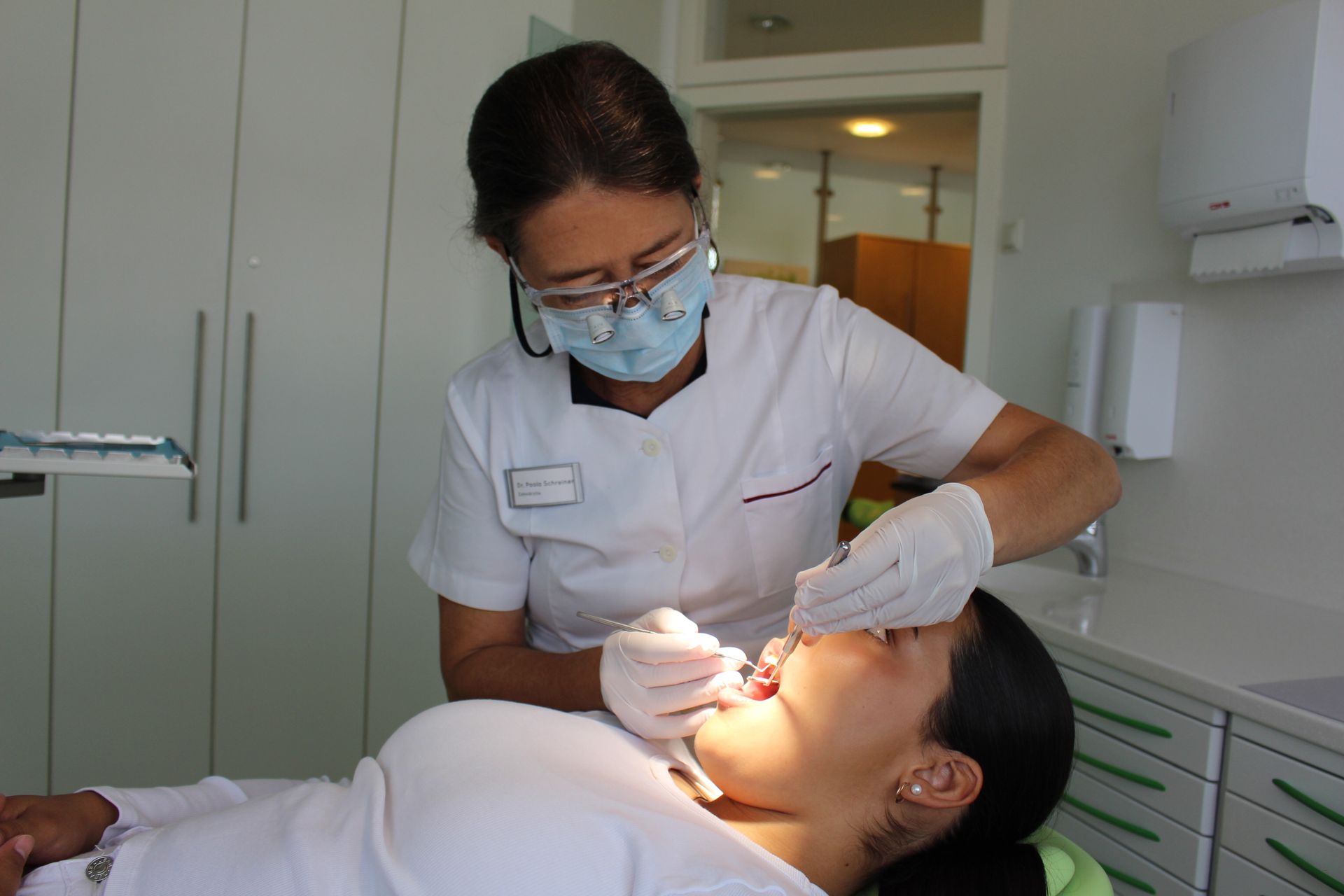 Ein junges Mädchen sitzt im Zahnarztstuhl und lässt ihre Zähne von einem Zahnarzt untersuchen.