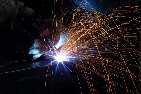 Welder at work, sparks flying from the intense blue light of the weld.