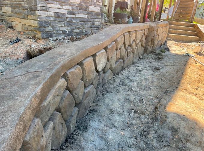 Stone retaining wall with curved concrete cap, under construction outdoors near steps.