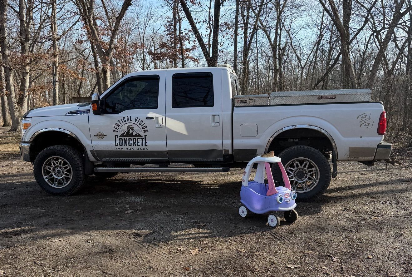 White pickup truck parked next to a child's toy car on a dirt road, trees in the background.