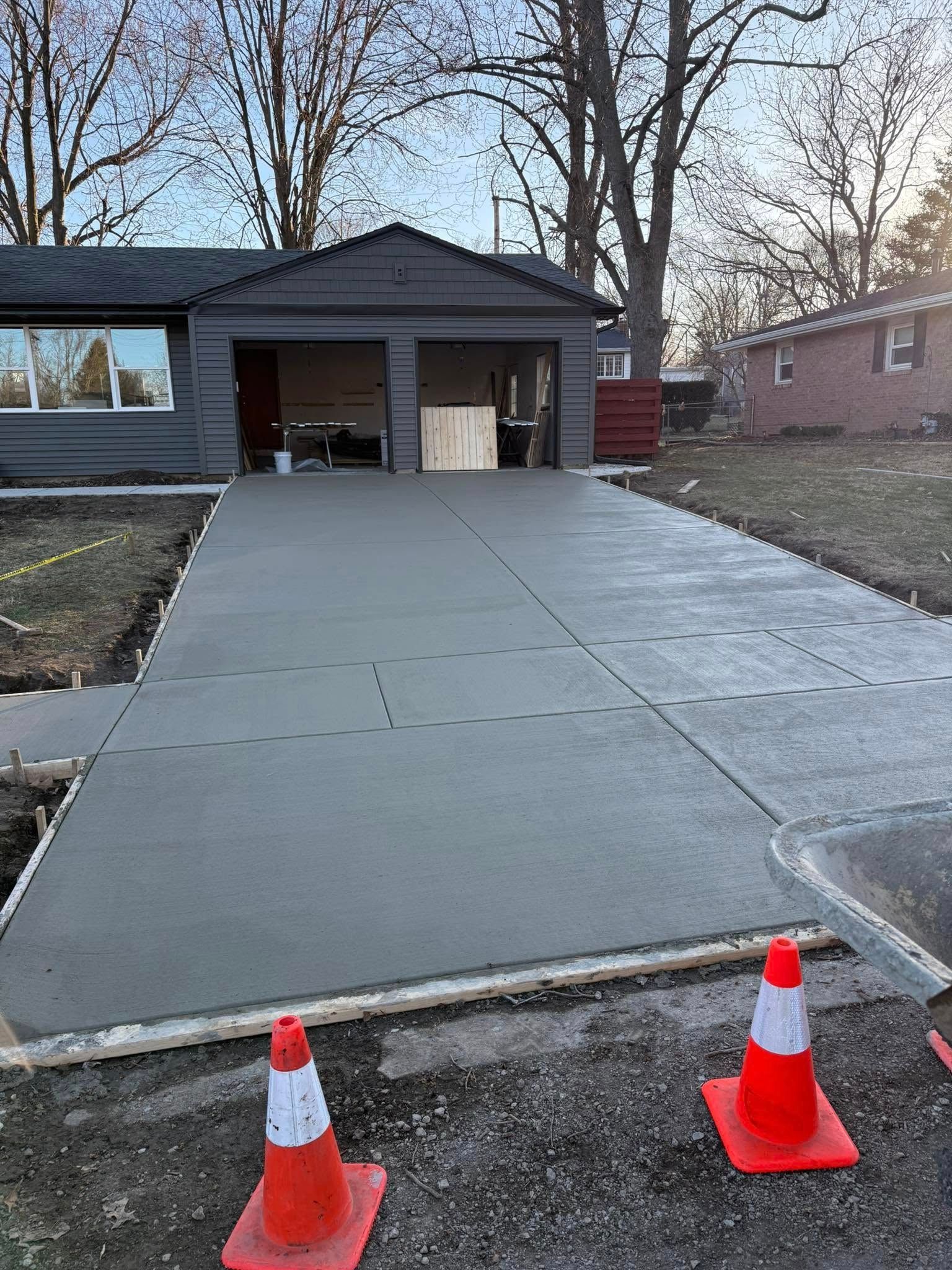 Freshly poured gray concrete driveway leads to a two-car garage. Orange cones mark the edges.