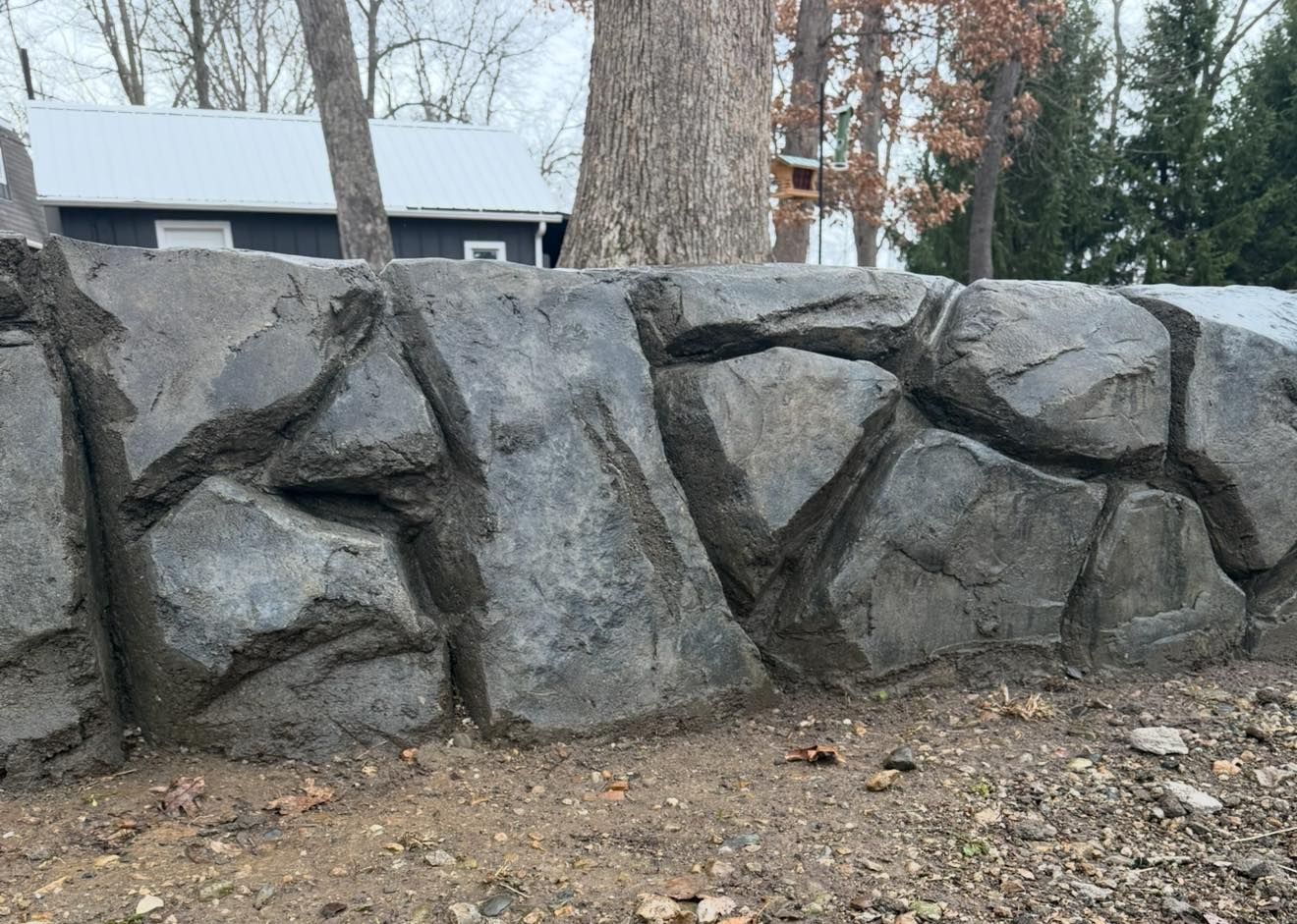 Newly poured concrete patio with brick retaining walls, steps, and a black fence in a backyard.