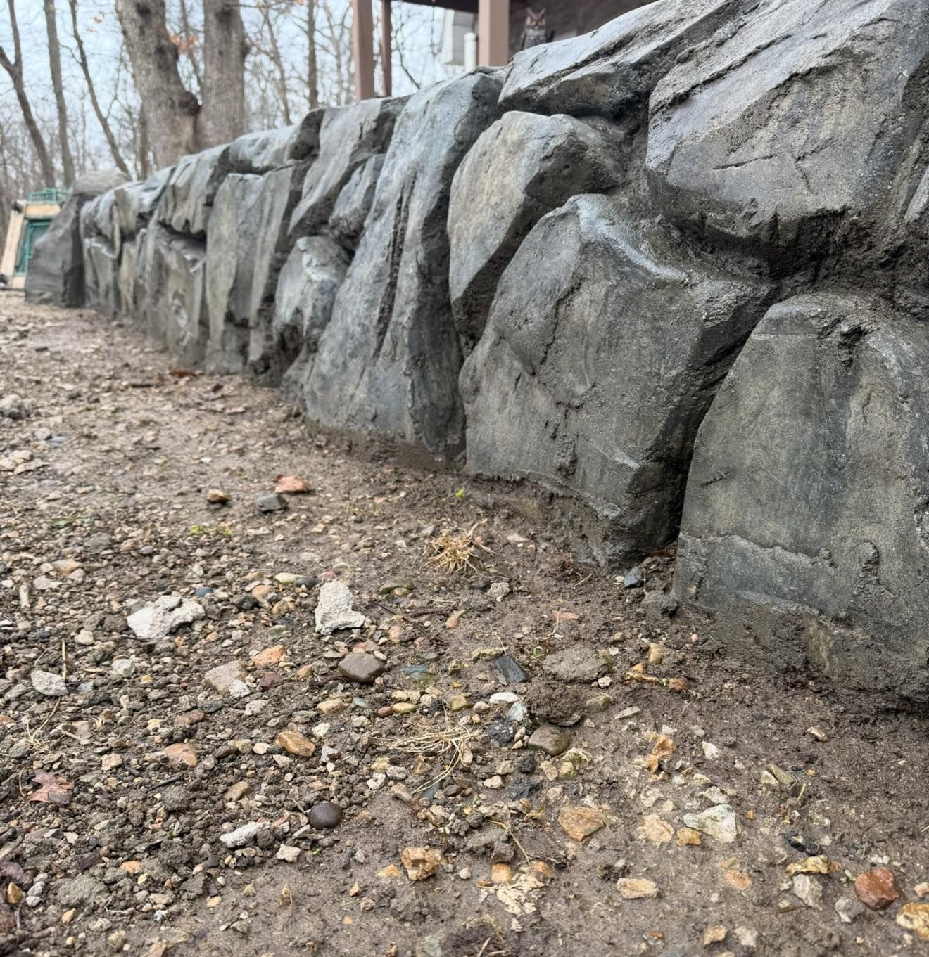Gray stone retaining wall along a dirt path, with a building in the background.