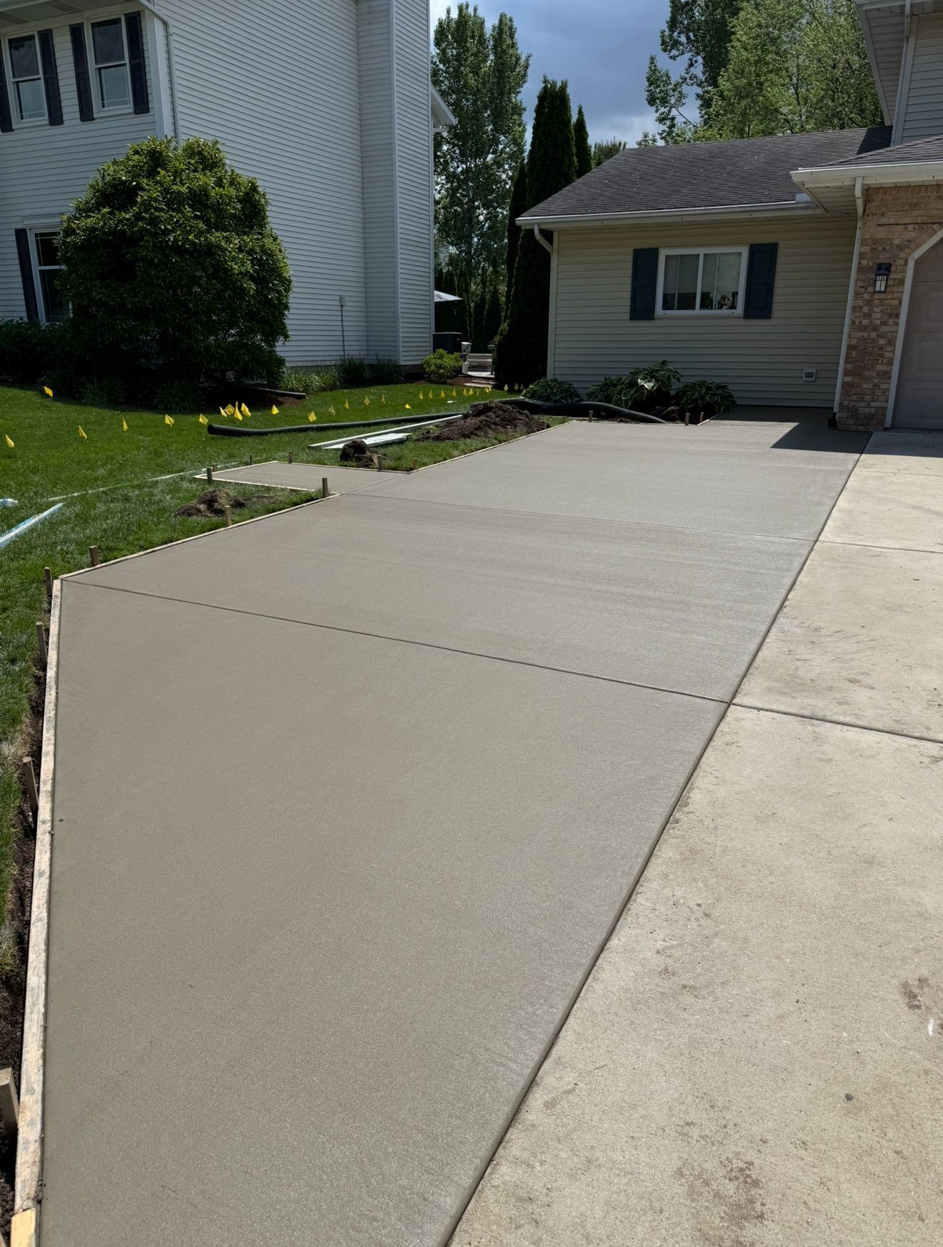 Freshly poured concrete driveway extension next to a house with a garage.